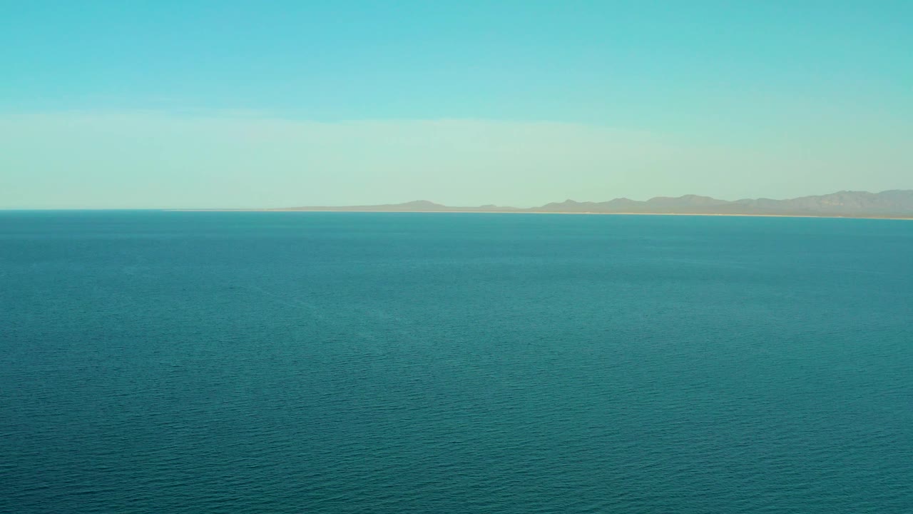 Mid-clip frame of calm blue water near El Sargento La Ventana, Mexico, with a level horizon, distant hills, soft daylight, and no visible people.
