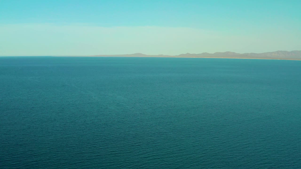 A wide turquoise sea view continues toward a narrow sandy coast and low mountains in El Sargento La Ventana, Mexico, with no boats or people visible.