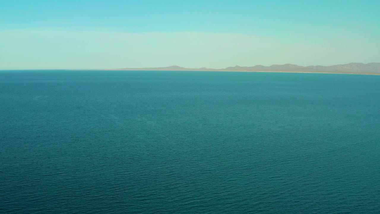 Blue-green water stretches to a distant beach and hazy low hills, with pale sky above and no visible people in the frame.