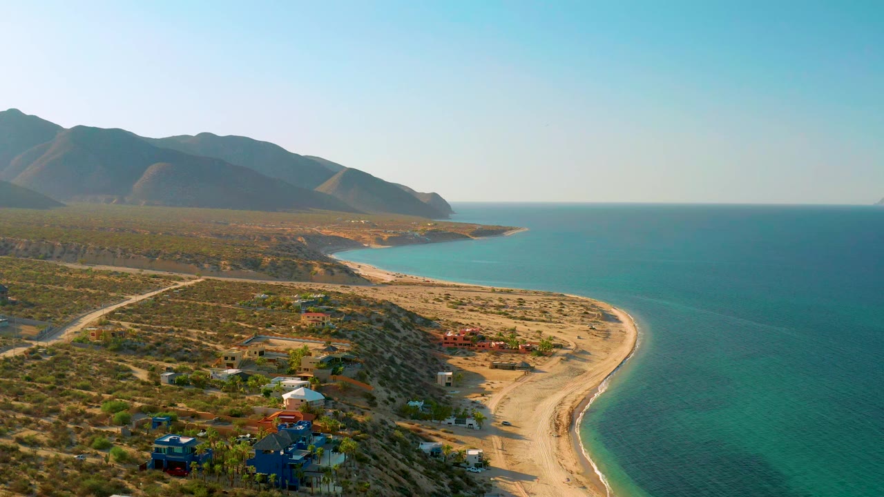 Drone-style view of beach, road, coastal homes, sea, and mountain ridge