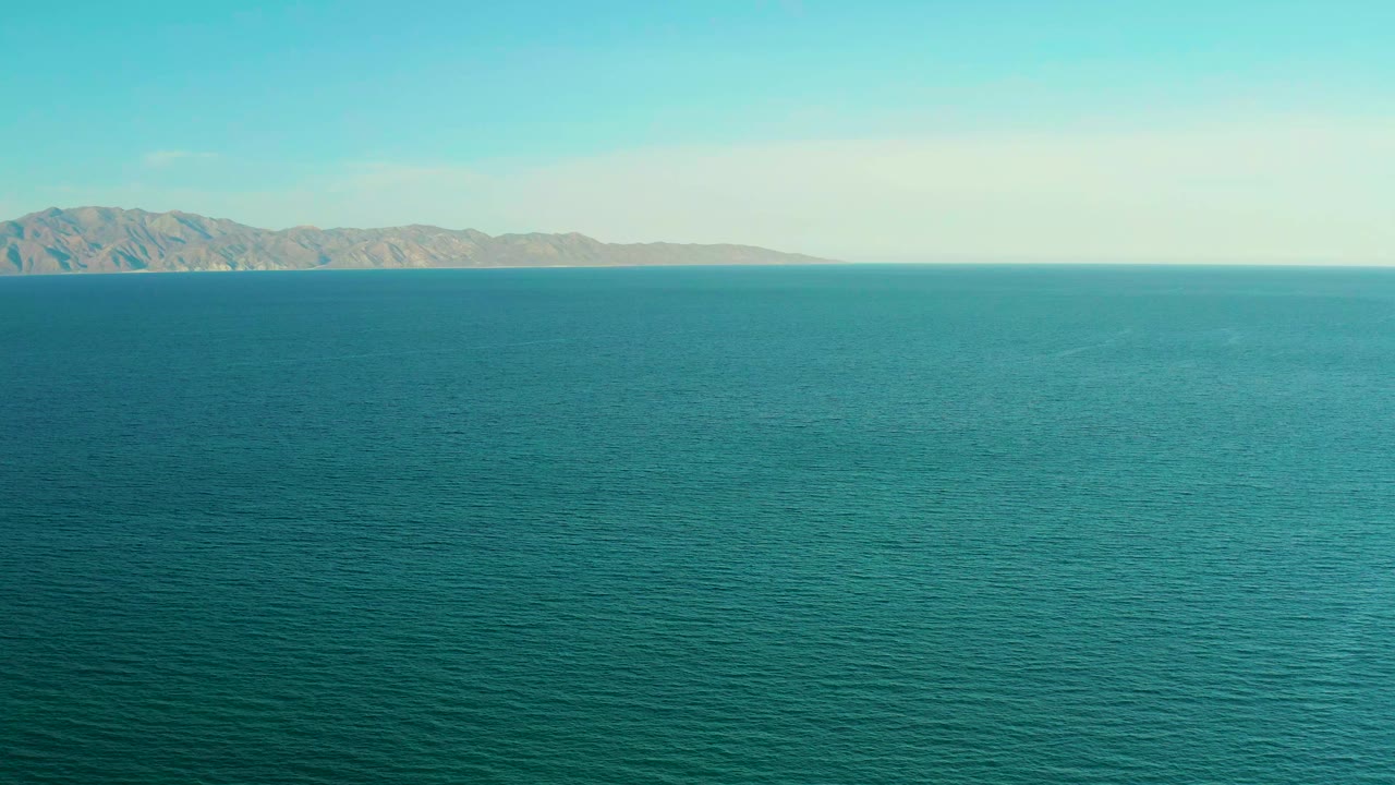 A wide view of textured teal water near El Sargento La Ventana, Mexico, with low mountains sitting along the upper-left horizon and no visible people.