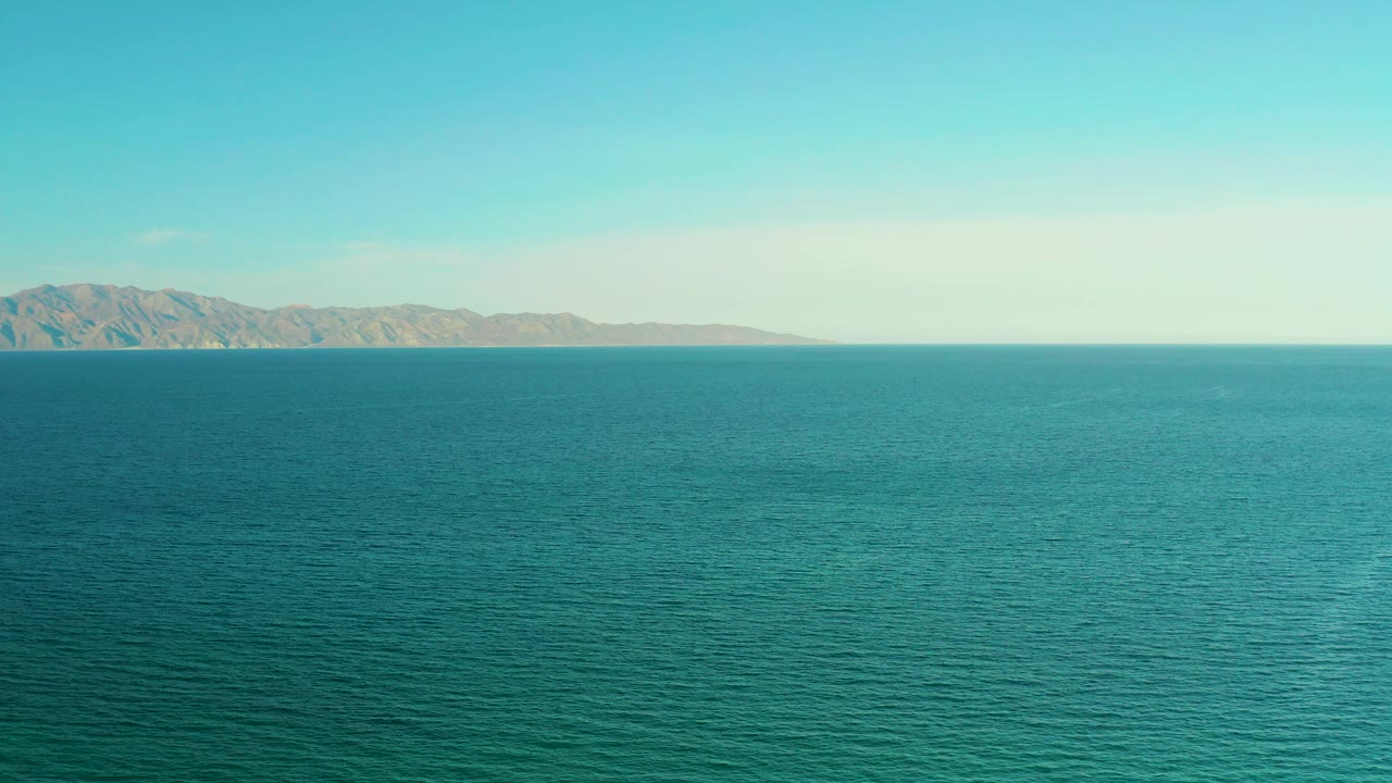Calm teal ocean in El Sargento La Ventana, Mexico, with the distant mountains stretched along the left side of the horizon and no visible people.