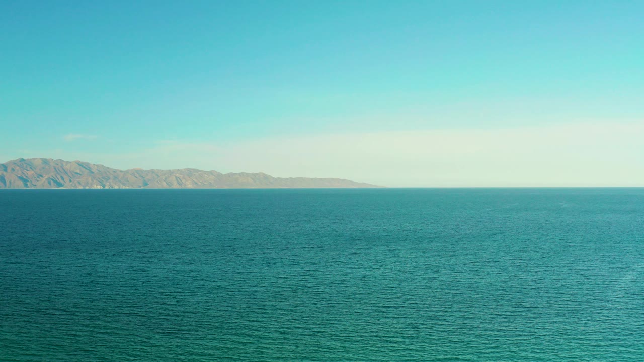 Wide blue ocean with distant mountains under a pale sky.