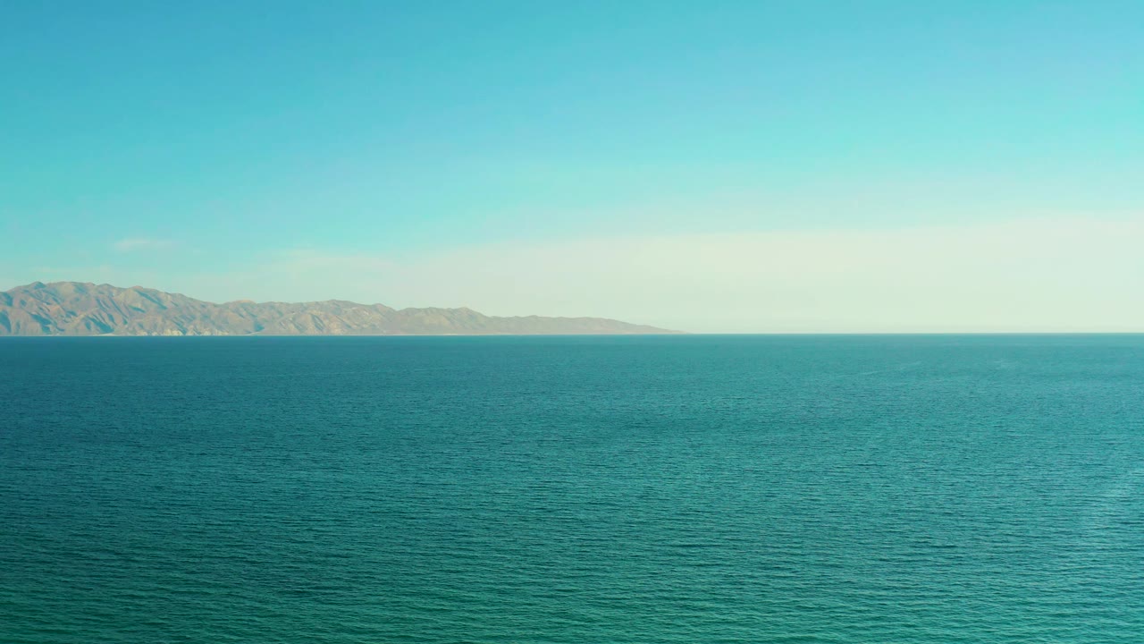 At 0:01, El Sargento La Ventana water fills the foreground while the mountain ridge sits slightly left of center beneath a clear pale sky, with no visible people.
