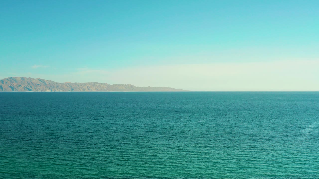 Opening frame of blue sea near El Sargento La Ventana, Mexico, with low tan mountains along the far horizon and no visible people.