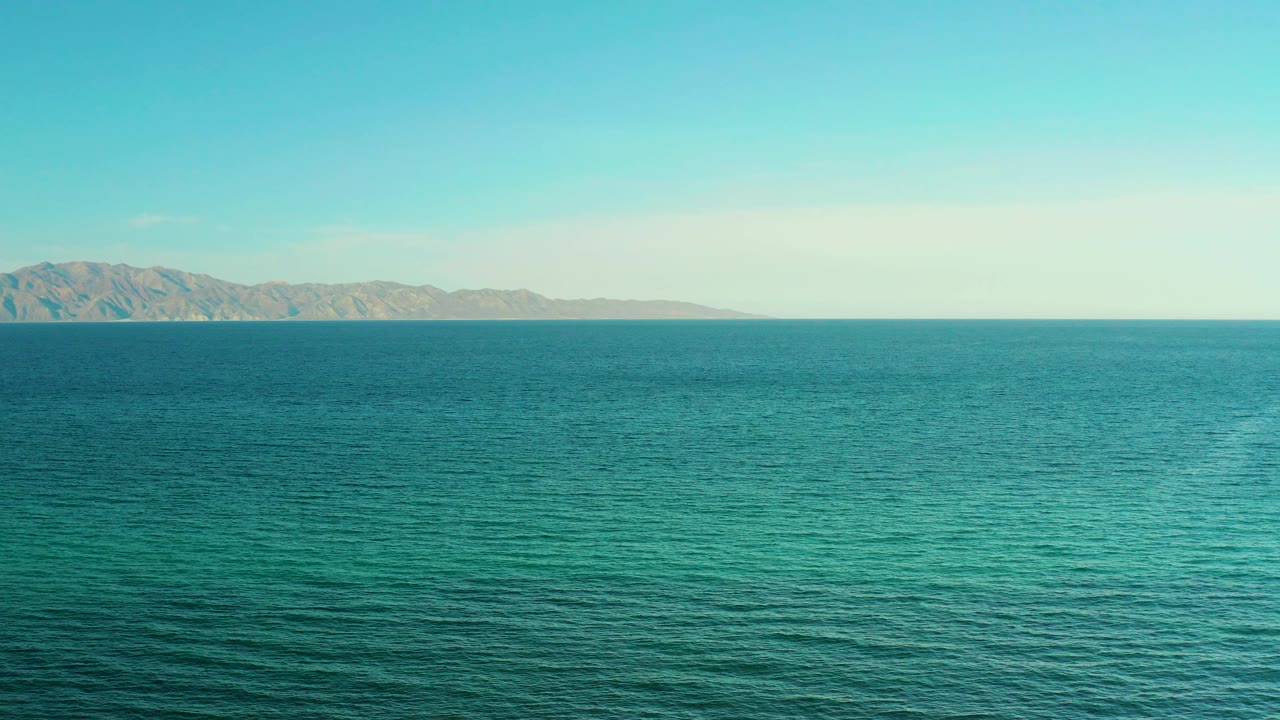 Blue ocean horizon with distant mountains under clear sky