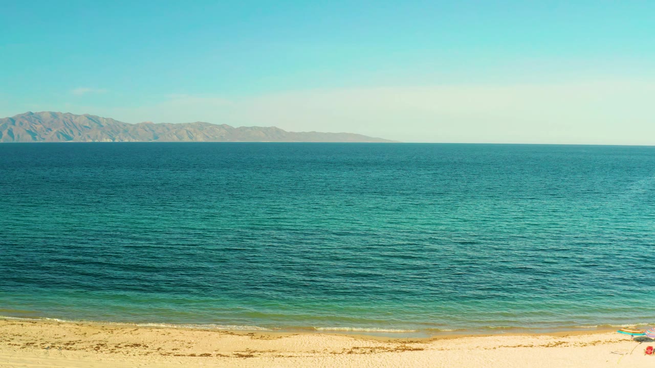 Calm shoreline with blue sea and mountains across the horizon