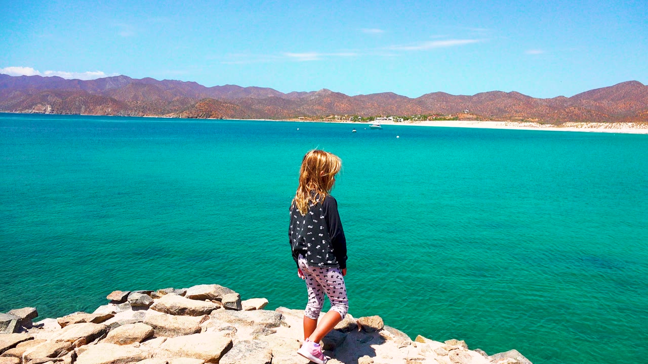 Girl walking along rocks with bright sea behind her