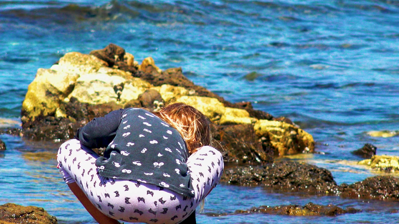 Child bent forward beside jagged shoreline rocks