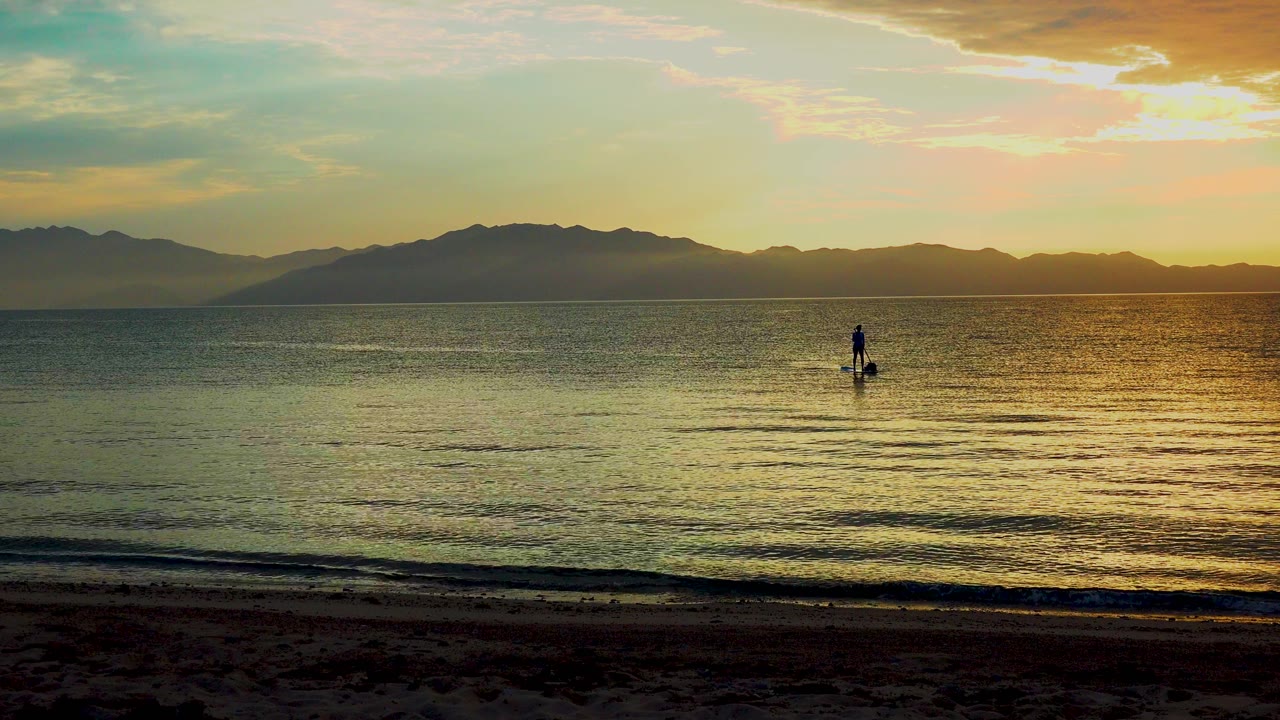 Wide water view with paddleboarder and dark mountain horizon.