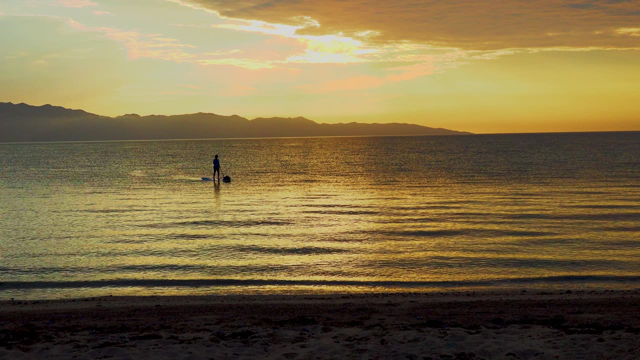 Distant paddle boarder centered on sunlit ocean water near shore.