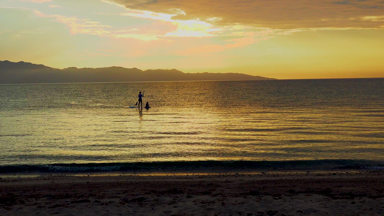 Distant paddleboarder on rippled sunset water.
