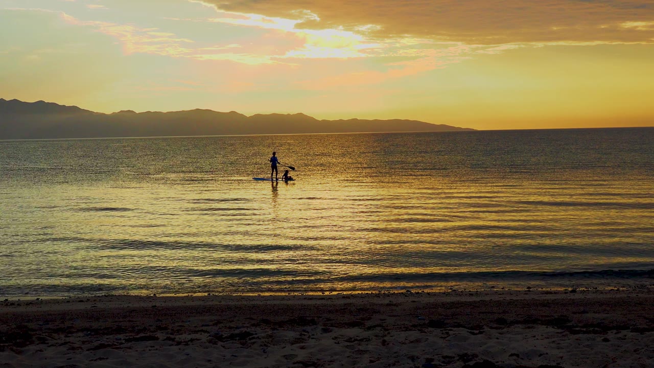 Silhouetted kayaker and gear remain near the center of calm sunset water.