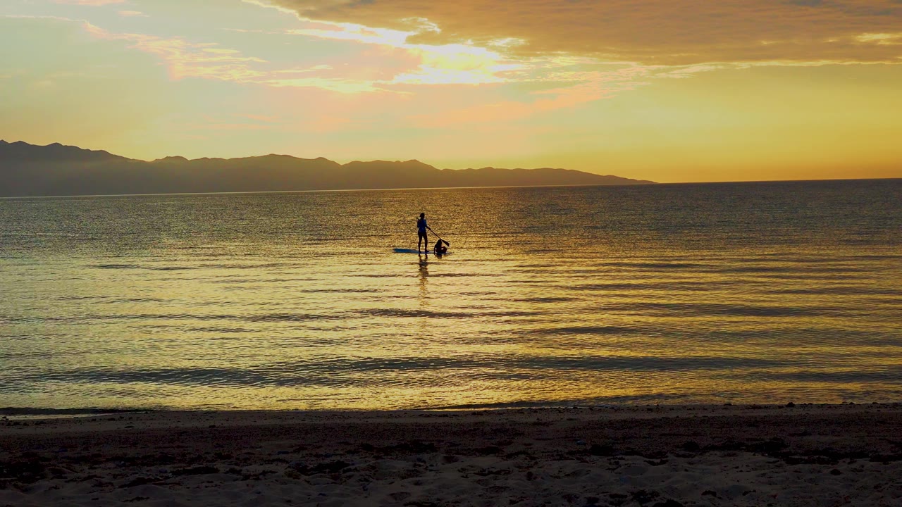 Silhouetted paddleboarder centered on reflective water with mountains behind.