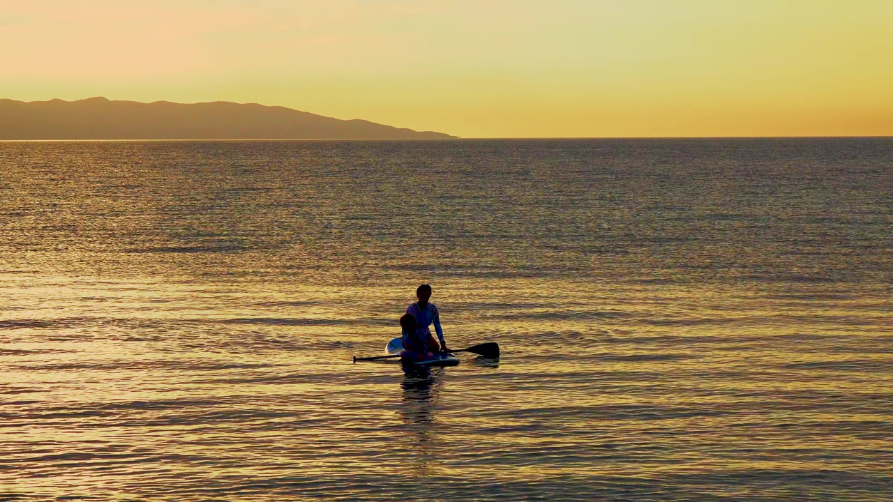A person rows a small boat across golden water in El Sargento La Ventana, Mexico, with low dark hills along the horizon at the start of the clip.
