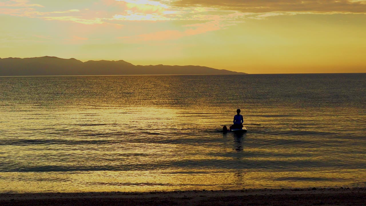 The paddler remains near the center of the El Sargento La Ventana waterline as yellow sunset reflections spread across rippled water.