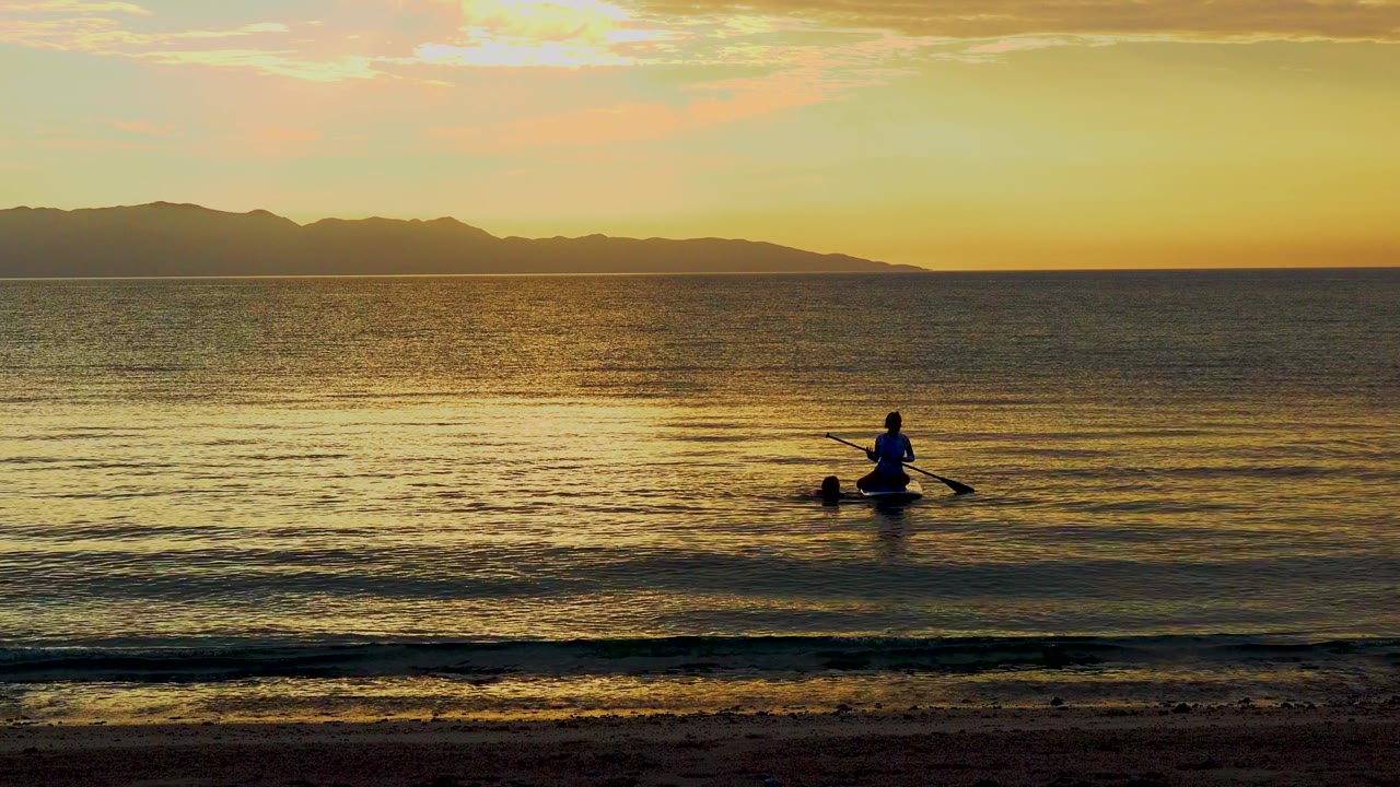 Paddler and paddle silhouette on golden water with low waves.