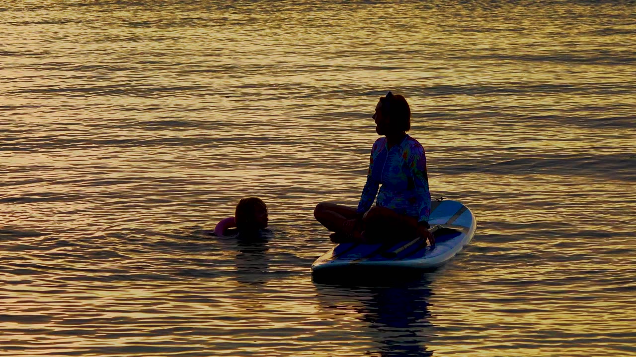 Silhouetted woman on a board with a child floating to the left.