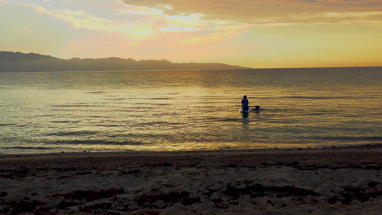 Distant paddleboarder on gold water beneath a sunset sky.