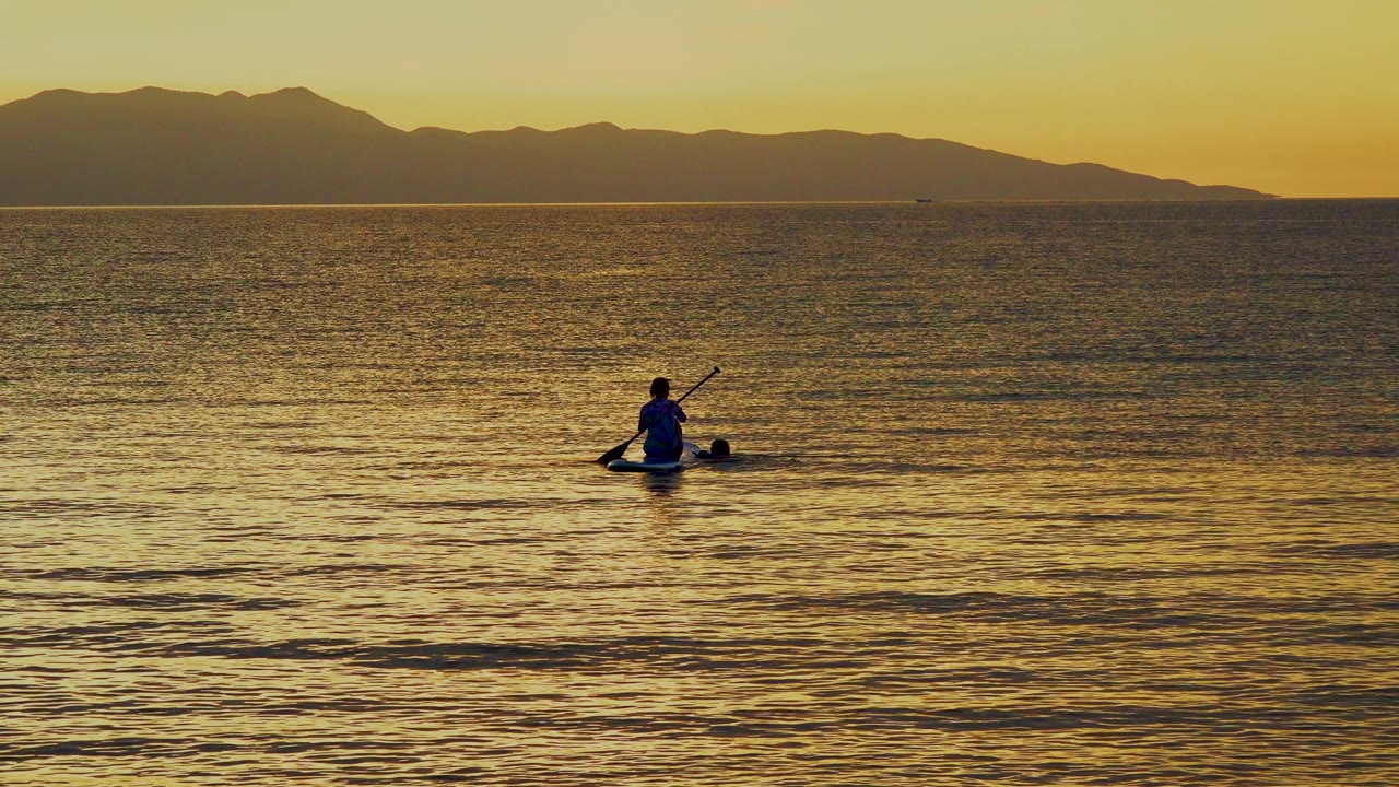 Small paddler centered on rippled golden sea below a mountain horizon.