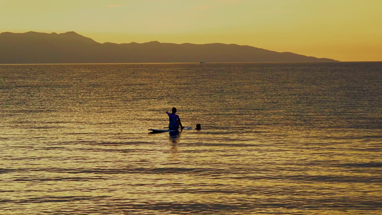 Paddle boarder near center on reflective water at sunset.