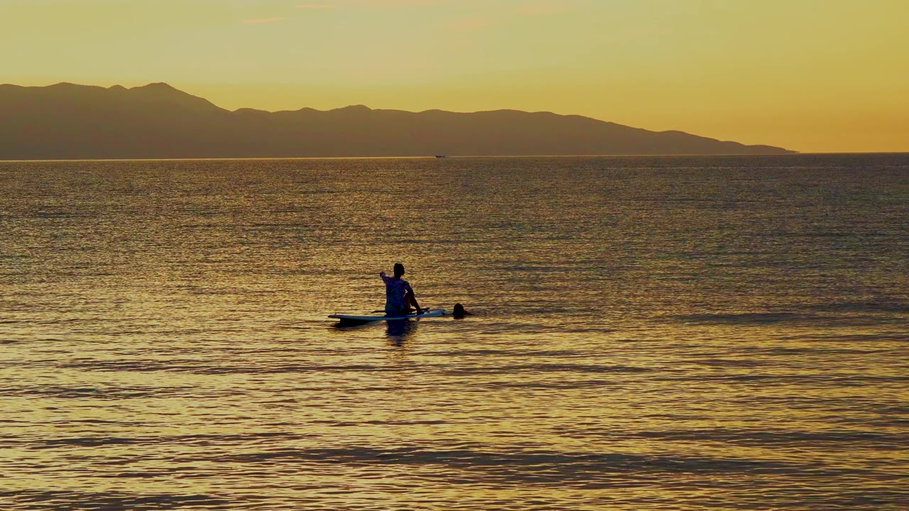 Paddle boarder low on water with sunset mountains behind.
