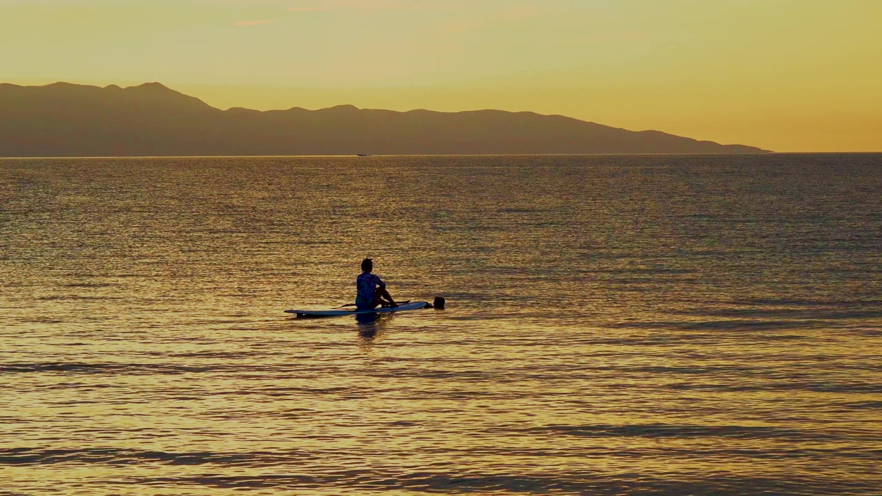 Distant canoeist on yellow sea with mountains on the horizon.