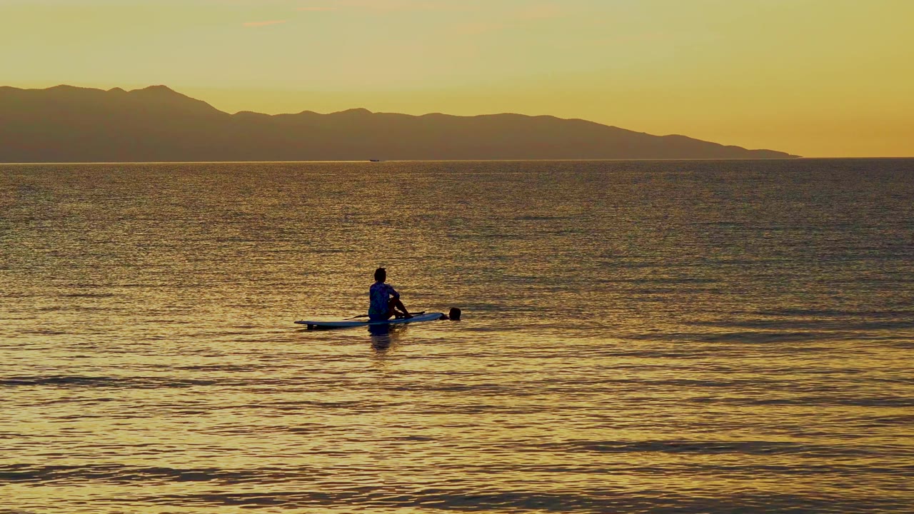 At 0:01 in El Sargento La Ventana, Mexico, the canoeist remains near center frame while small surface ripples catch yellow light below the dark coastline.