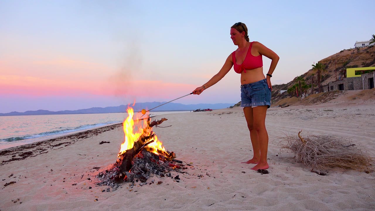 Woman leaning a roasting stick toward a bonfire.