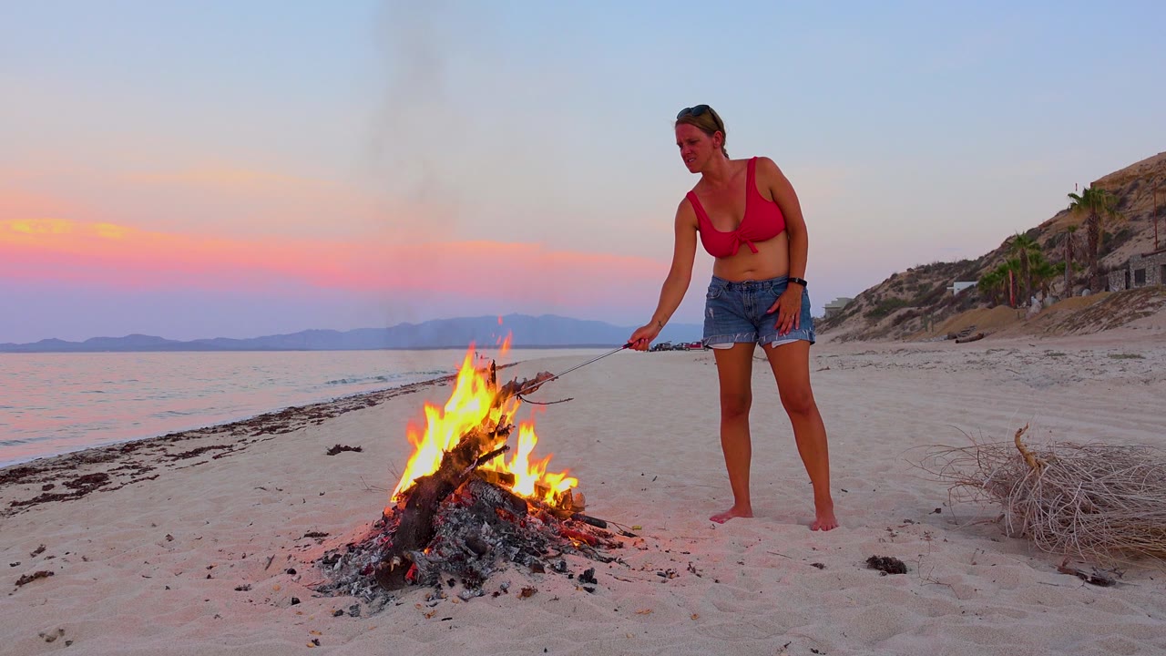 Woman leans toward a campfire on the sand.