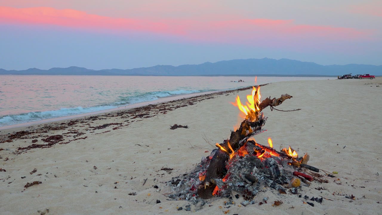Beach campfire close to camera with pastel sunset horizon