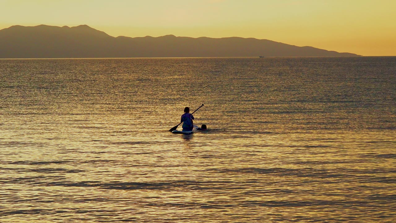 Lone paddler centered on rippled water below a mountain horizon.