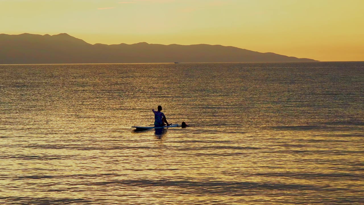 The kayak sits low against a broad expanse of water, with small shoreward ripples in the foreground and a dark mountain ridge beyond the horizon.