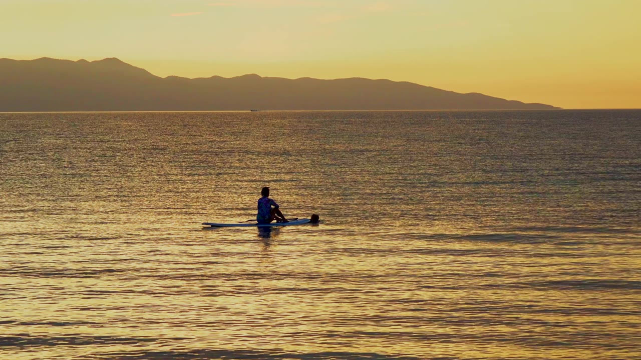 A single person on the small watercraft sits low in frame at El Sargento La Ventana, Mexico, while the orange sky and shadowed mountains define the background.
