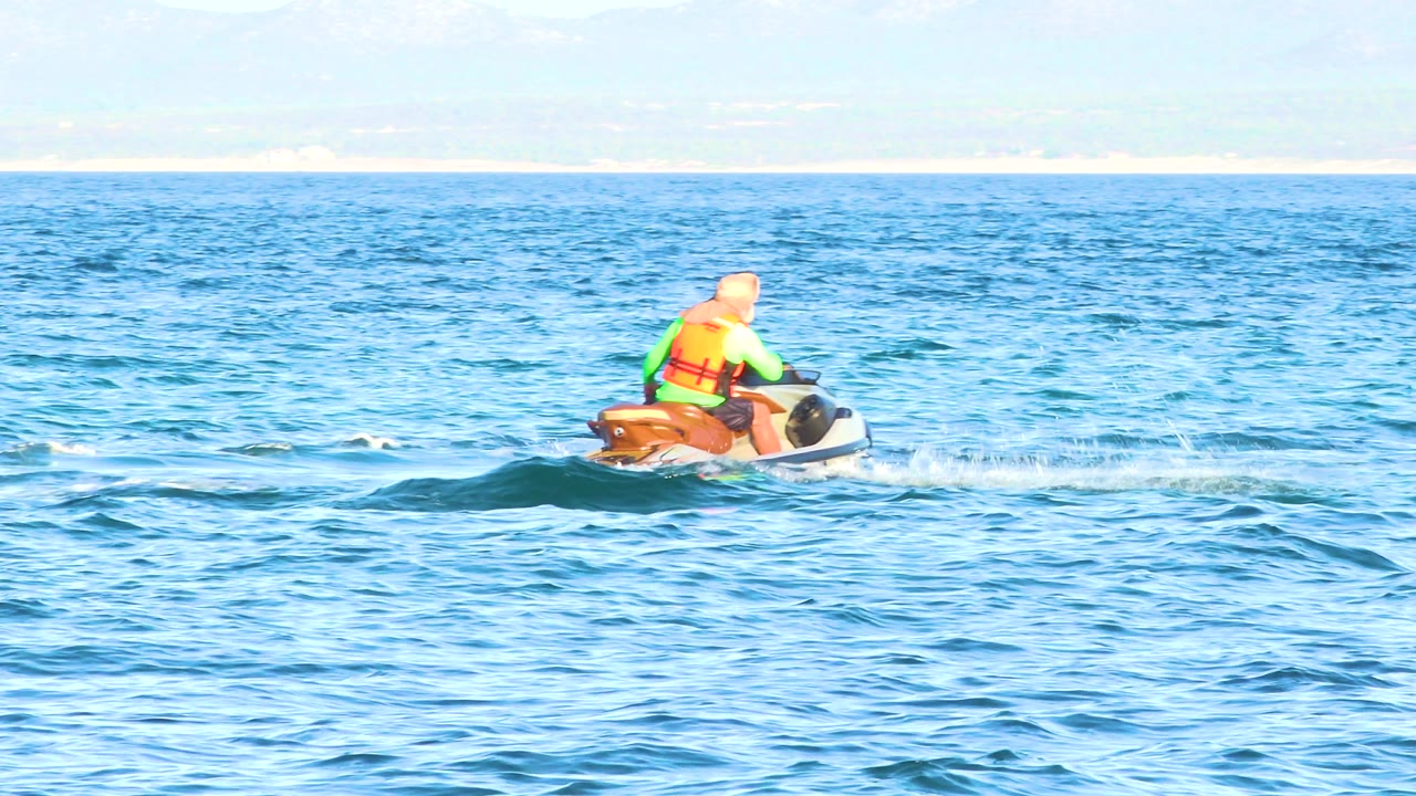 Jet ski rider crossing small waves with spray behind the craft.