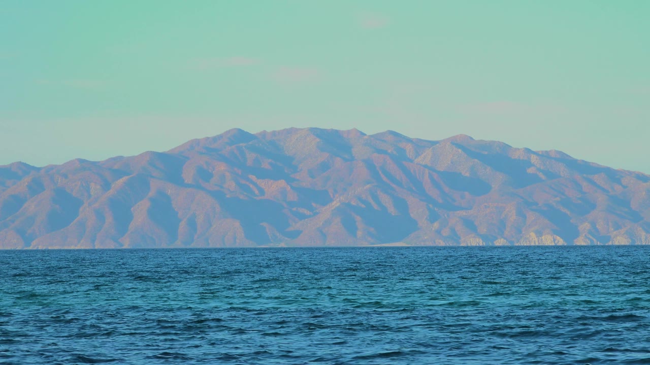 Opening frame of rippling blue water facing distant mountains in El Sargento La Ventana, Mexico, with pale sky and no visible people.