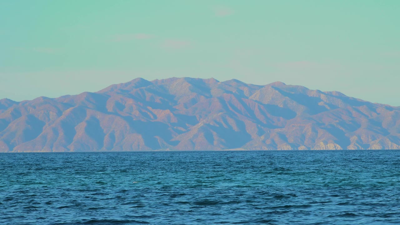 Low coastal view of waves with mountains in the distance.