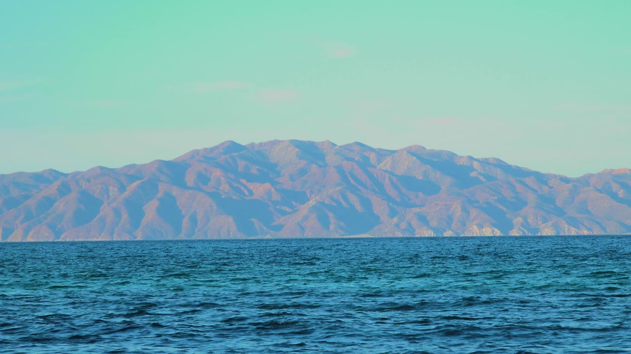 Opening frame of El Sargento La Ventana, Mexico, with rippled blue water in front of a hazy mountain range and no visible people.