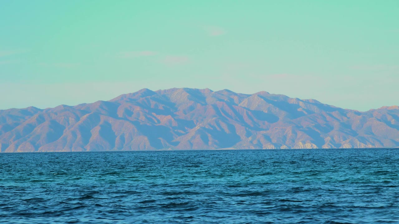 One second in, the foreground water shows shifting dark wave texture while the distant El Sargento La Ventana mountain line stays fixed, with no visible people.