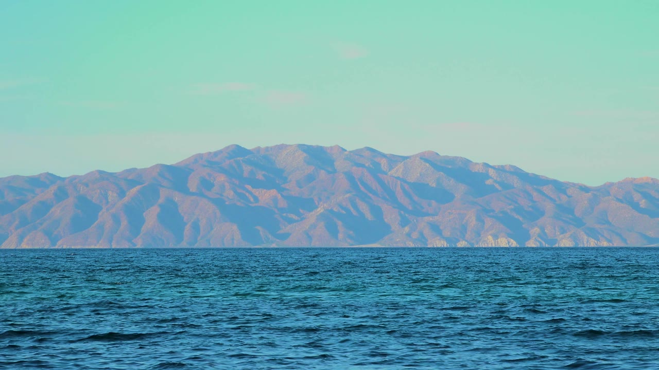 Blue ocean water below distant mountains and pale sky.