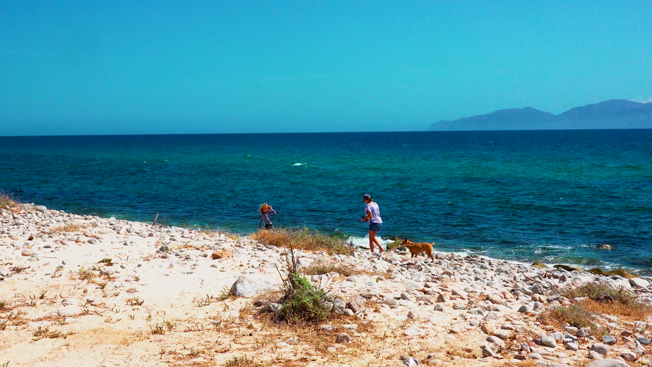 Woman, child, and dog continue along the rocky shoreline.