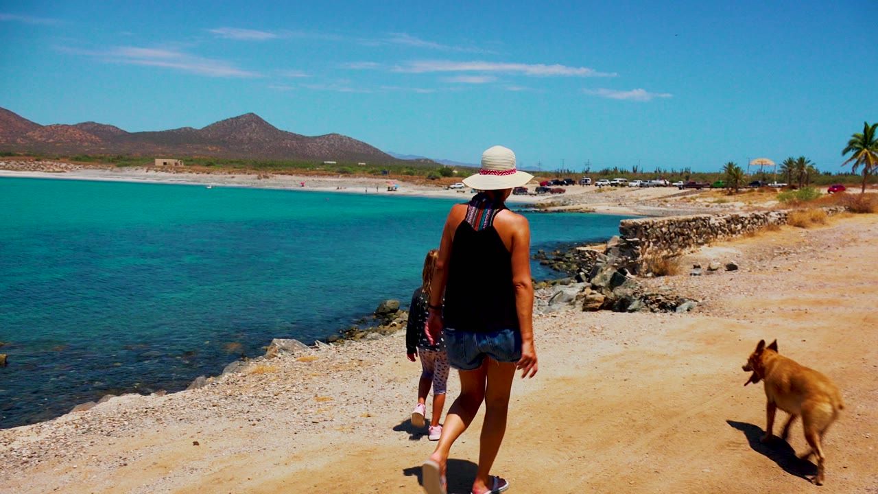 Woman and child ahead on a sandy waterfront path with a dog nearby.