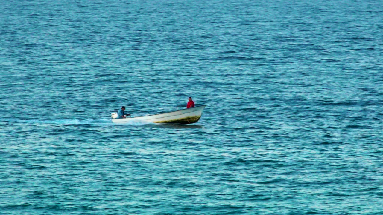 At 0:00, a small white motorboat with two distant people rides across rippled blue water in El Sargento La Ventana, Mexico.