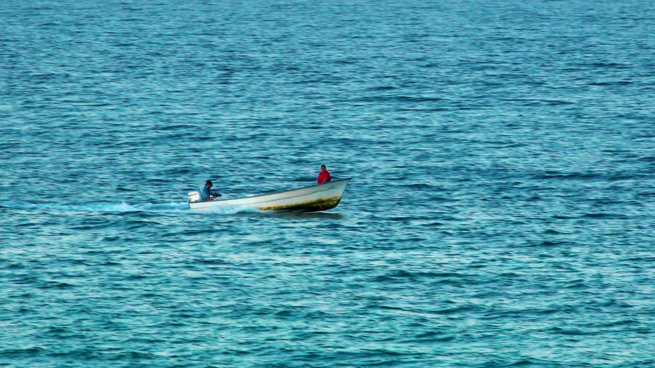 Motorboat carrying two people over textured turquoise water.
