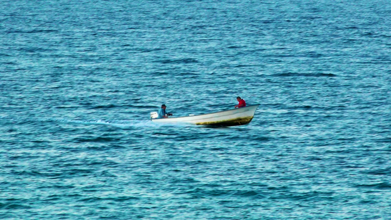 Two people ride a small boat across rippled blue water.
