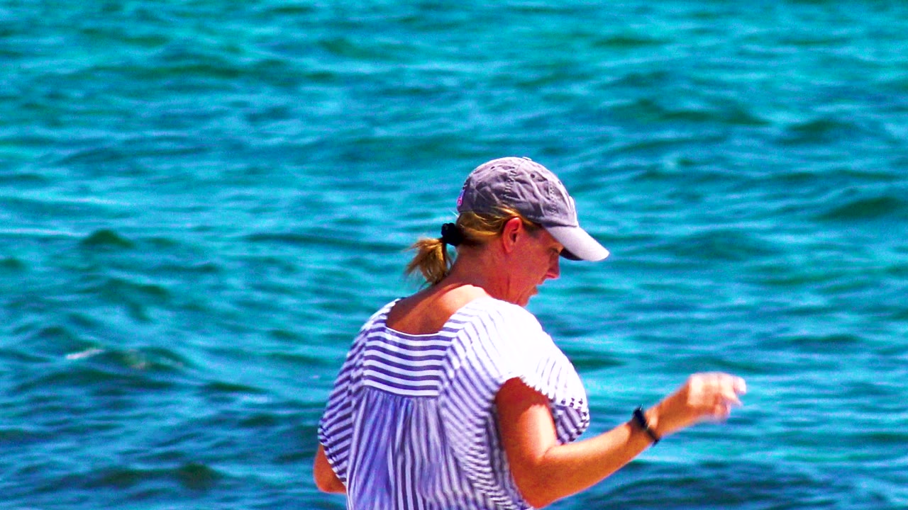 Woman walking with hand raised near turquoise water