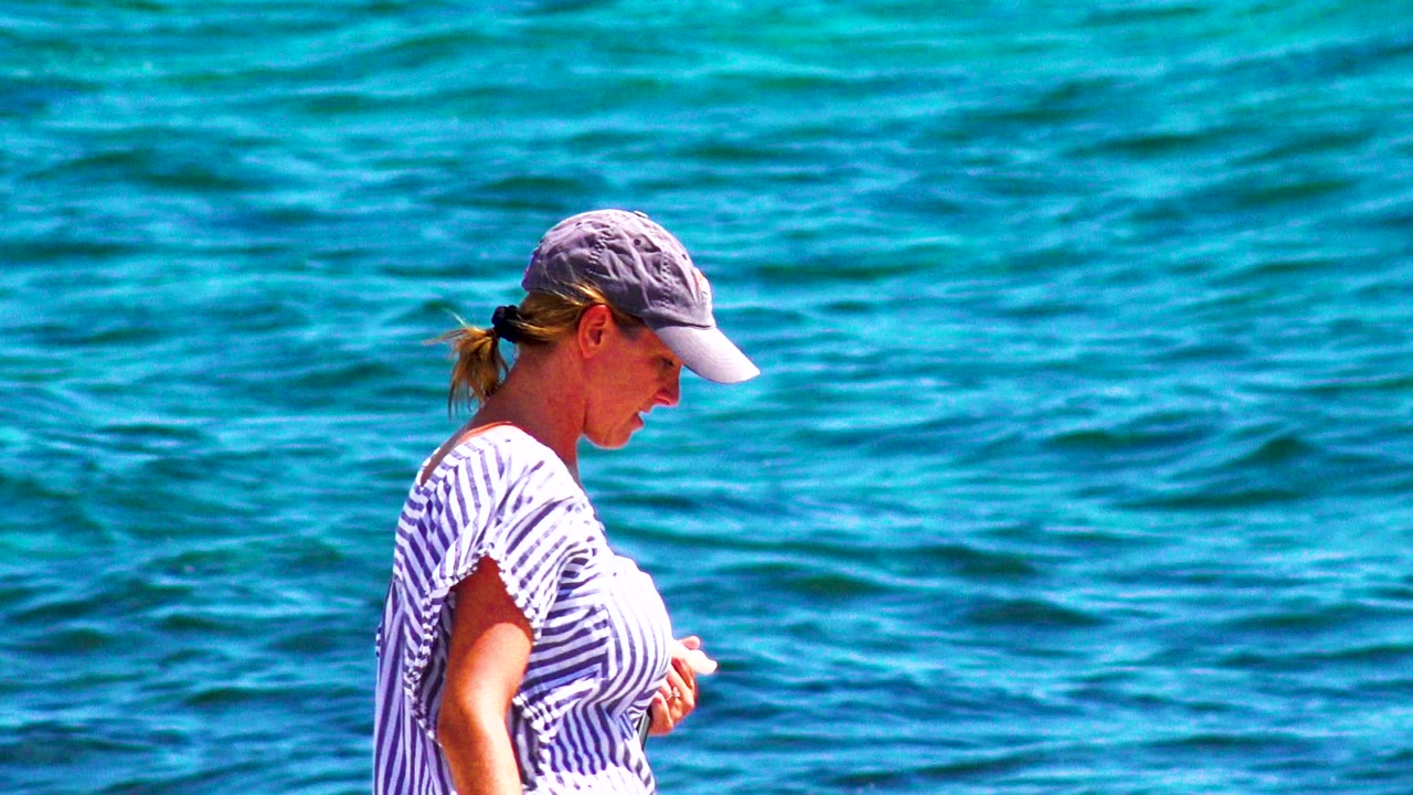 Woman in striped shirt beside textured blue water.