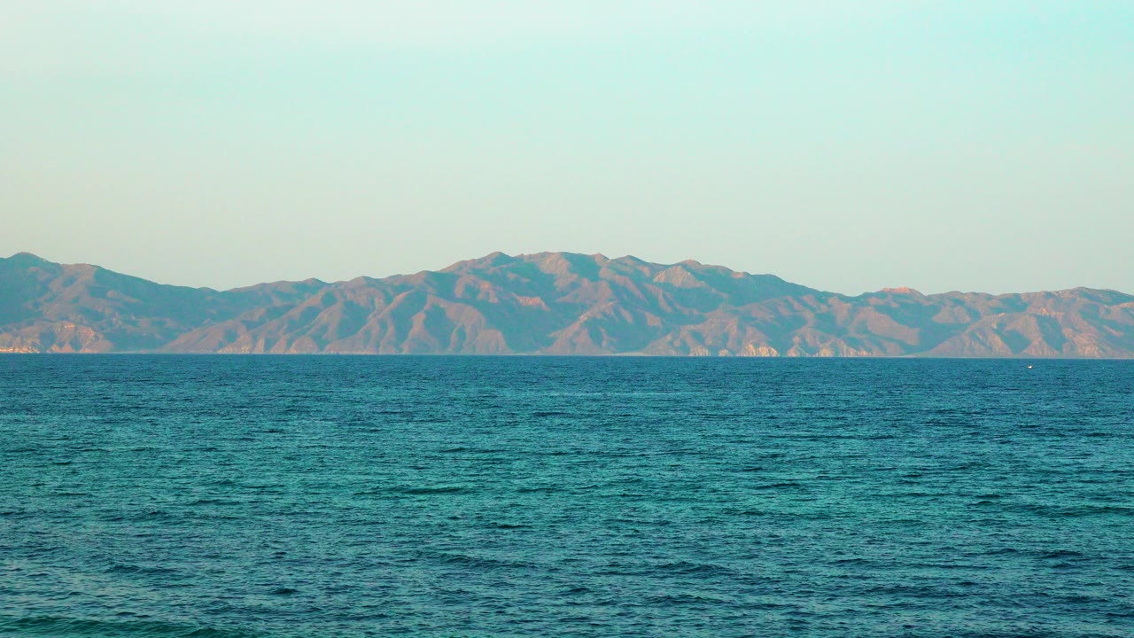 Blue ocean texture fills the lower frame while hazy mountains stretch across the horizon, with no visible people or boats.