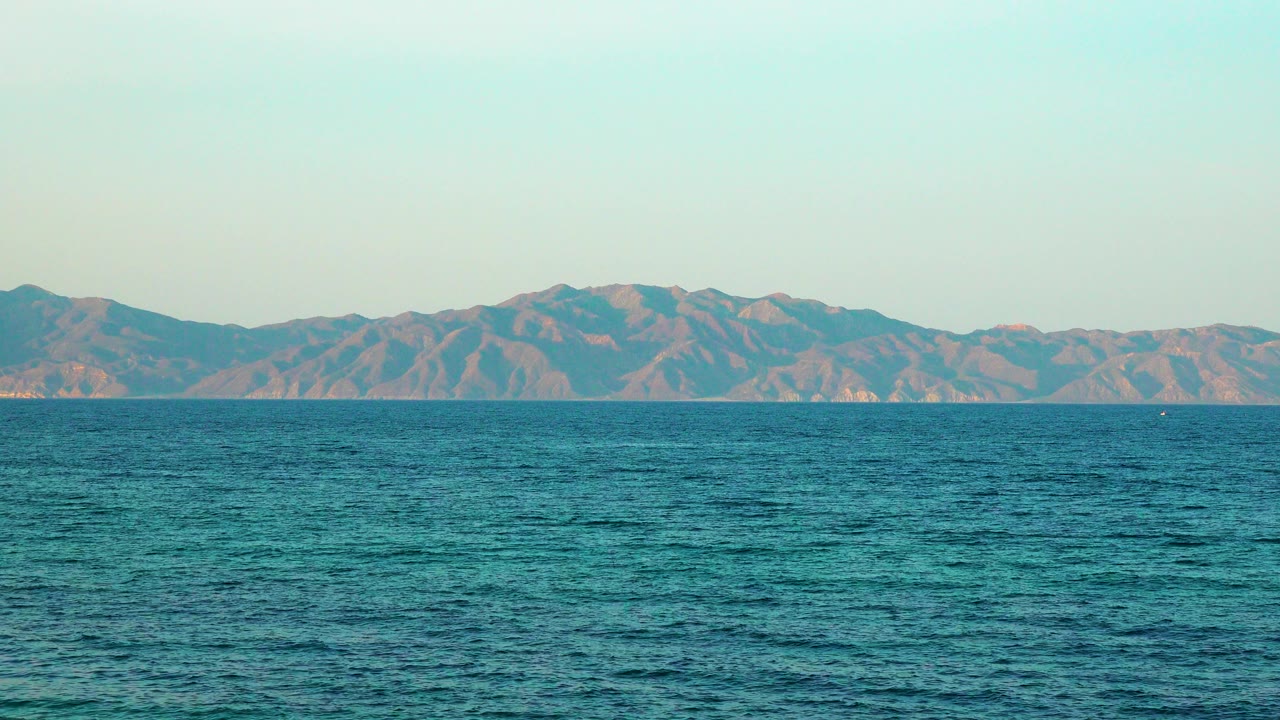 Small ripples pattern the ocean surface while the mountain range remains low across the horizon, with no visible people or animals.