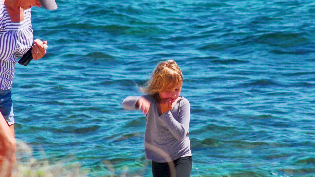 Child moving beside turquoise water with adult partly visible.